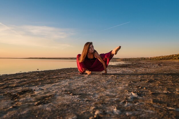 Kobieta na plaży o zachodzie słońca zaczyna robić trening asan jogi. Poranny trening rozgrzewkowy z naturalnym rozciąganiem