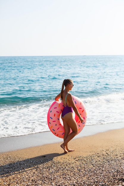 Kobieta na plaży spaceruje z dmuchanym pierścieniem po morzu, spaceruje relaksując się w tropikalnym raju dla relaksu. Młoda modelka do opalania na letnie wakacje.