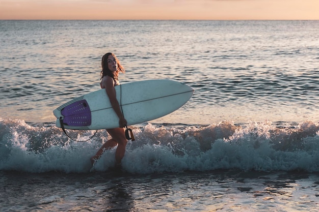 Kobieta na plaży z deską surfingową pod pachą z zimnym wyrazem twarzy