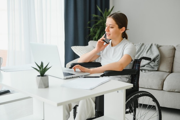 Kobieta na wózku inwalidzkim pracuje na laptopie w domowym biurze z psem asystującym jako towarzyszem