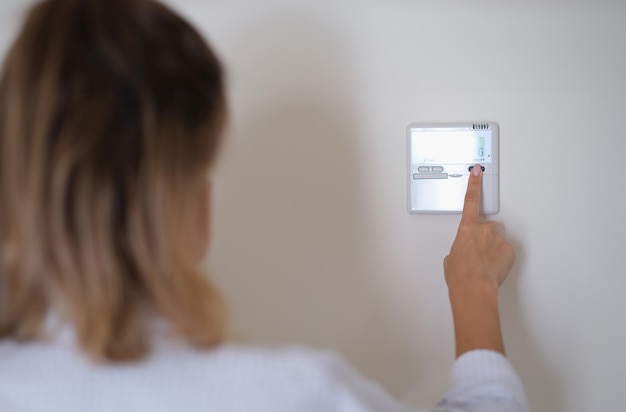 Zdjęcie kobieta naciskająca przycisk zdalnego sterowania klimatyzatorem w zbliżeniu do ściany