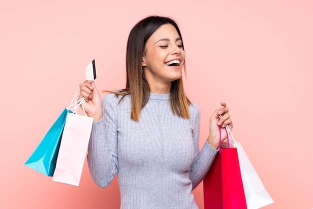 Kobieta nad różową ścianą trzyma torby na zakupy i kartę kredytową