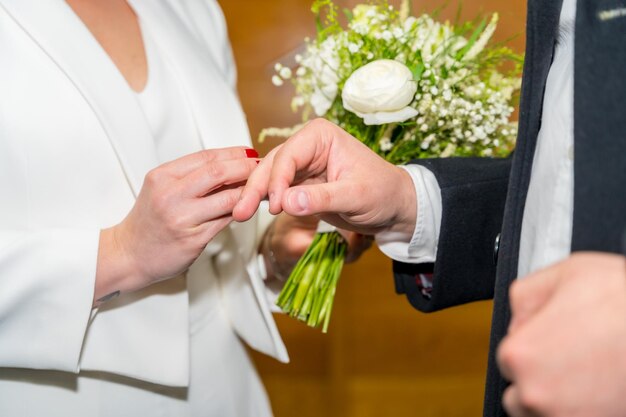 Zdjęcie kobieta nakłada pierścionek panowi młodemu na ceremonii ślubnej