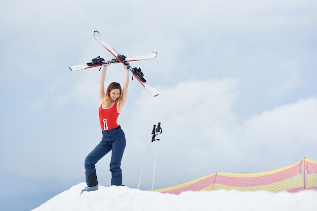 Kobieta narciarz stojący na szczycie zaśnieżonego wzgórza ze sprzętem narciarskim