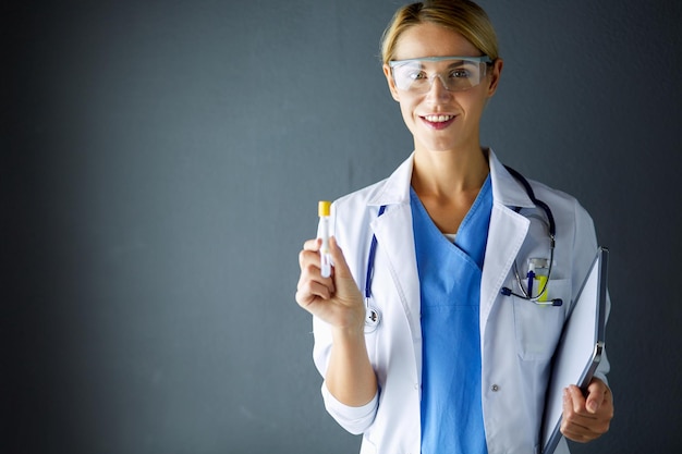 Kobieta naukowiec medyczny lub naukowy lub lekarz patrzący na probówkę z klarownym roztworem w laboratorium lub laboratorium