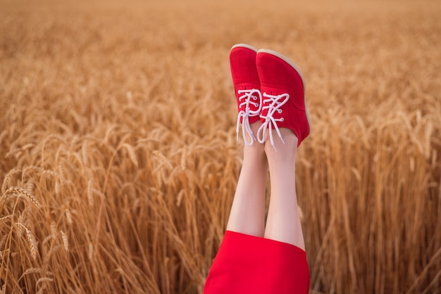Kobieta nogi w czerwone buty śmieszne wystaje na tle pola pszenicy.