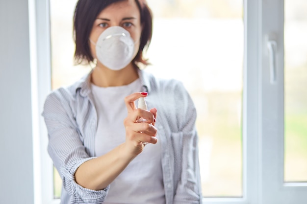 Kobieta nosi maskę higieniczną i naciska alkohol w sprayu, aby chronić, dezynfekować. Koncepcja koronawirusa, covid-19 i ochrony przed zanieczyszczeniami. Zostań w domu.