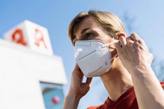 Kobieta nosząca maskę antywirusową, aby chronić innych przed zakażeniem koronawirusem COVID19 i SARS cov 2 przed sklepem aptecznym