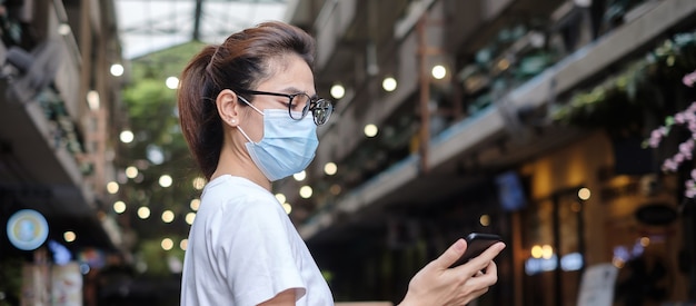 Kobieta nosząca medyczną maskę na twarz i korzystająca ze smartfona podczas spaceru po nocnym targu, zapobiegaj koronawirusowi lub chorobie Corona Virus (Covid-19). Zdrowie, koncepcja życia