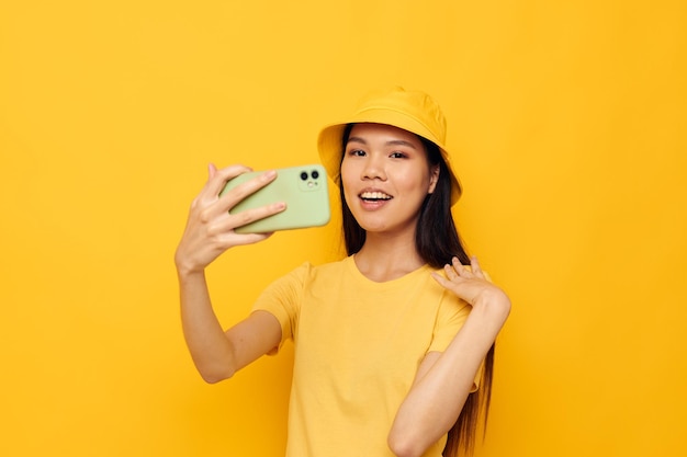 Kobieta o azjatyckim wyglądzie rozmawiająca przez telefon pozuje niezmienione modne żółte tło