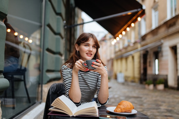 kobieta o brązowych włosach wysyła wolny czas na tarasie kawiarni ze smaczną kawą i papierową książką