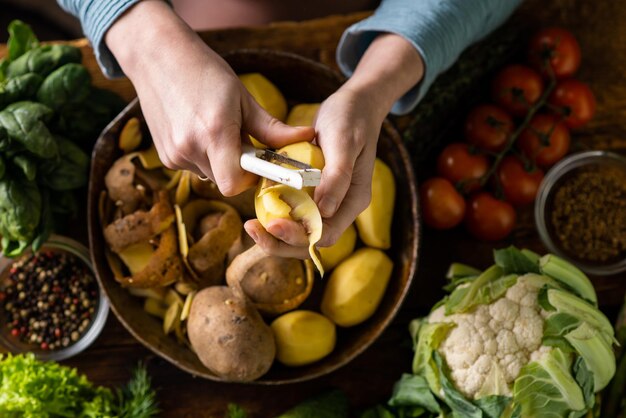 Kobieta obiera ziemniaki Różne świeże warzywa leżą na stole Gotowanie potraw wegetariańskich