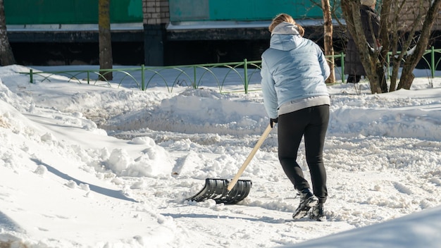 Kobieta odgarnia śnieg z chodnika.
