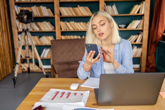 Kobieta odnosząca sukcesy w biznesie używa smartfona pracującego zdalnie z domowego biura siedzącego