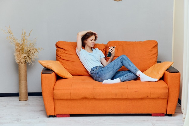 Kobieta odpoczywa na pomarańczowej sofie obok technologii telefonicznej