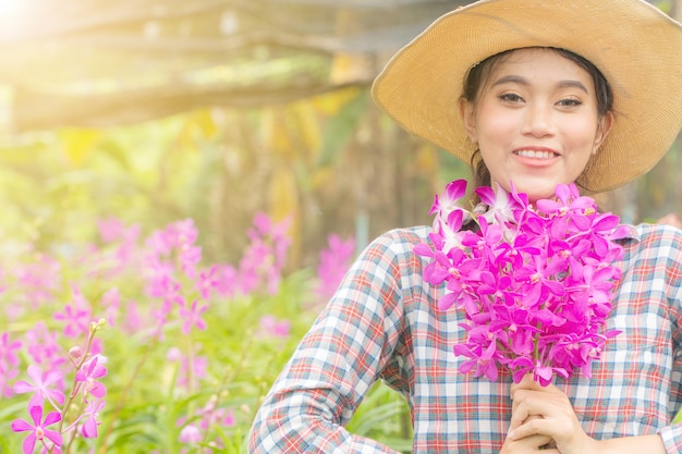 Kobieta Ogrodnik Ubrany W Koszulę W Kratę W Kapeluszu Trzyma Różową Orchideę W Ręku.