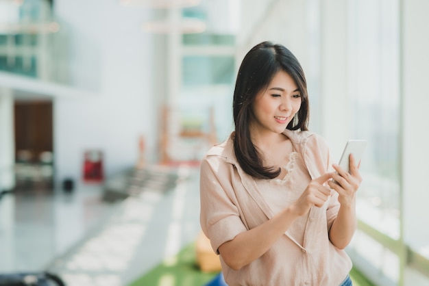 Kobieta ono uśmiecha się podczas gdy używać smartphone w nowożytnym biurze