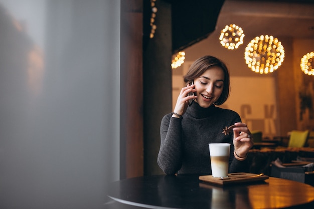 Kobieta opowiada na telefonie i pije kawę w kawiarni