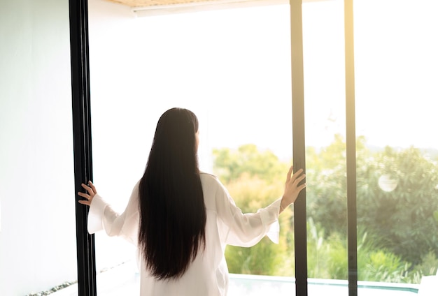 Kobieta otwiera szklane drzwi, aby złapać poranne słońce i świeże powietrze w Koh Larn Resort Pattaya