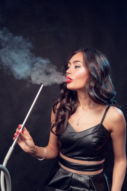 kobieta pali fajkę / piękna czarująca kobieta w czarnej sukni pali fajkę
