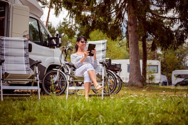 Kobieta patrząca na tablet w pobliżu kempingu. Wakacje w przyczepie kempingowej. Rodzinna podróż na wakacje, wyjazd na wakacje w kamperze RV. Technologia komunikacji informacyjnej połączenia Wi-Fi.