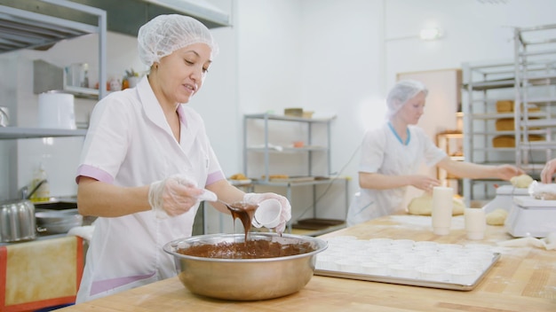 Kobieta piekarz miesza krem czekoladowy w metalowej misce i robi ciasta, z bliska