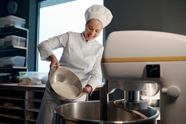 Kobieta piekarz nalewa mąkę do mieszarki w piekarni