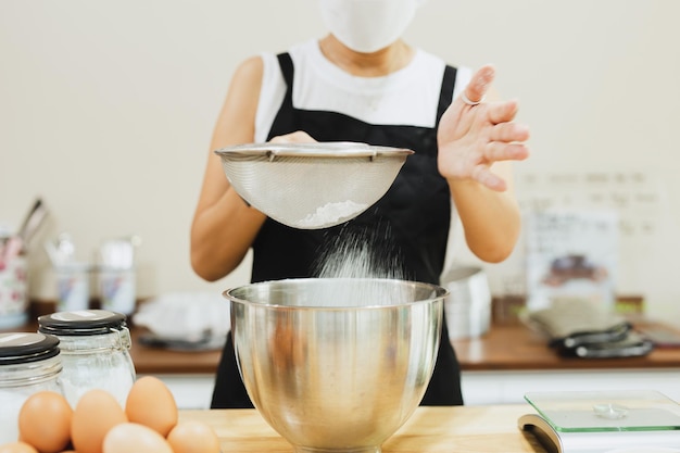 Kobieta piekarz przesiewa mąkę do miski