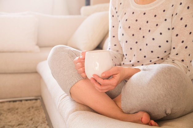 Kobieta pijąca filiżankę kawy lub herbaty siedząca przytulnie w domu Relaks