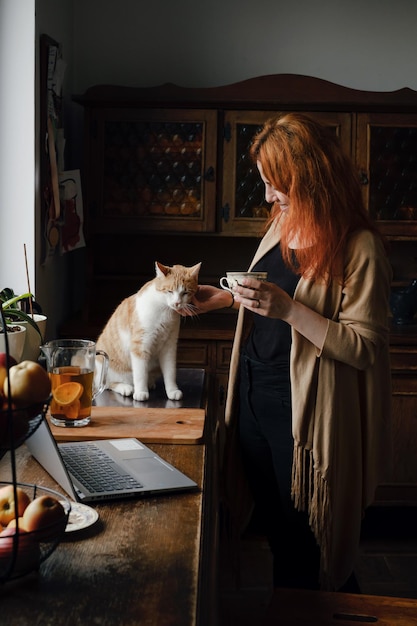 Kobieta pijąca herbatę i głaszcząca rudego kota w domu retro