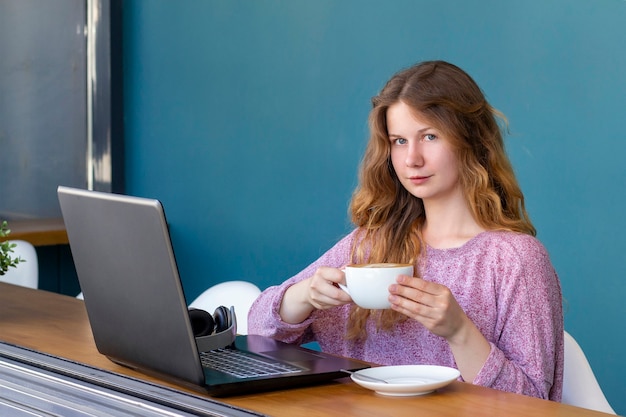 Kobieta pije kawę w kawiarni i za pomocą laptopa