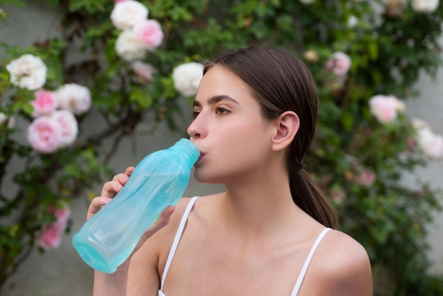 Kobieta pije wodę z butelki sportowej, wykonując ćwiczenia rozciągające na świeżym powietrzu