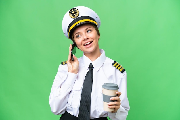 Kobieta pilot samolotu nad odizolowanym tłem klucza chrominancji trzymająca kawę na wynos i telefon komórkowy