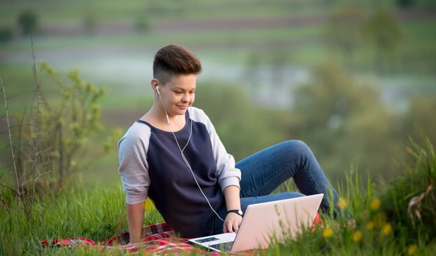 Kobieta pisać na maszynie na jej laptopie pracuje outdoors siedzieć na trawie