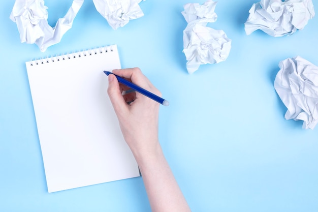 Zdjęcie kobieta pisze w notatniku wokoło zmiętego papieru, błękitny tło