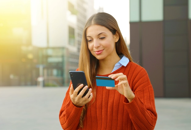 Kobieta płaci online smartfonem i kartą kredytową na zewnątrz