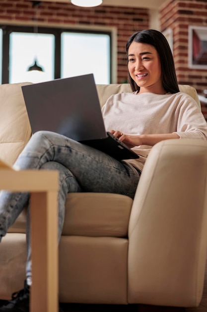 Kobieta pochodzenia azjatyckiego pracująca w domowym biurze przy użyciu technologii laptopa komputerowego sieci internetowej online zdalnego internetu szukanie pracy w mediach społecznościowych przeglądanie wiadomości czytanie plotek