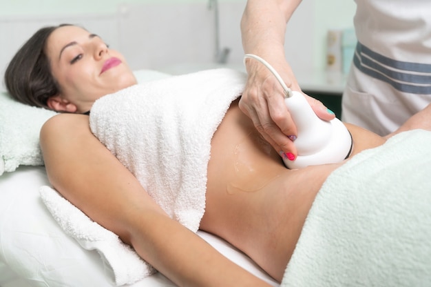 Kobieta poddana zabiegowi kawitacji ultradźwiękowej przez kosmetolog klientkę korzystającą z antycellulit ...