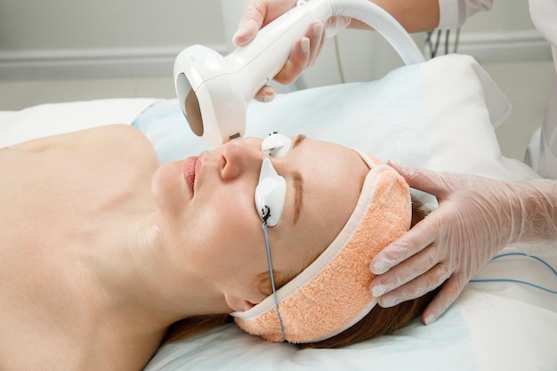 Kobieta poddawana laserowemu zabiegowi na twarz w klinice kosmetologicznej opracowywana jest koncepcja odmładzania skóry peeling laserowy