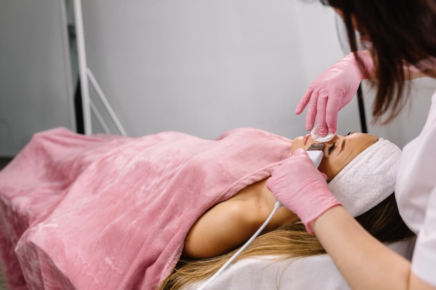 Kobieta poddawana terapii oczyszczającej profesjonalnym aparatem ultradźwiękowym w gabinecie kosmetologicznym