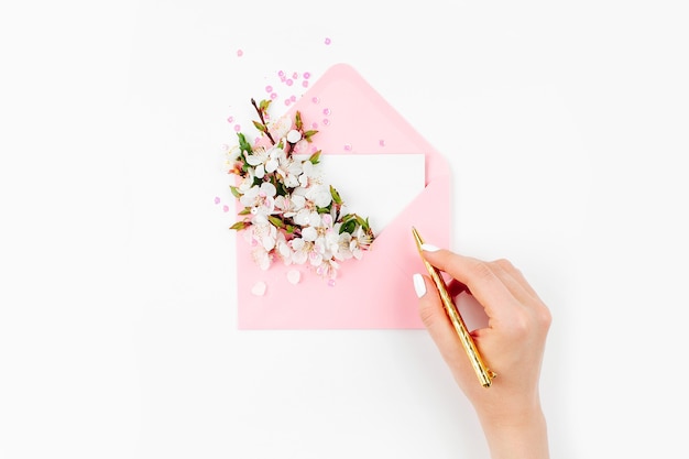 Kobieta podpisująca kartę. Różowa koperta z pustą kartą i wiosenną kompozycją kwiatową. Płaski świeckich, widok z góry.