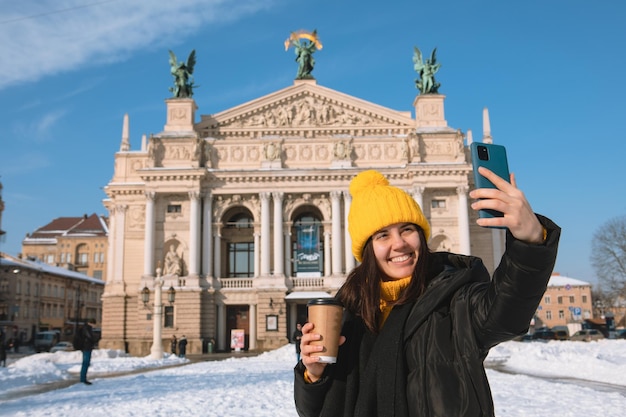 Kobieta podróżnik pije kawę, aby zrobić selfie przed budynkiem opery