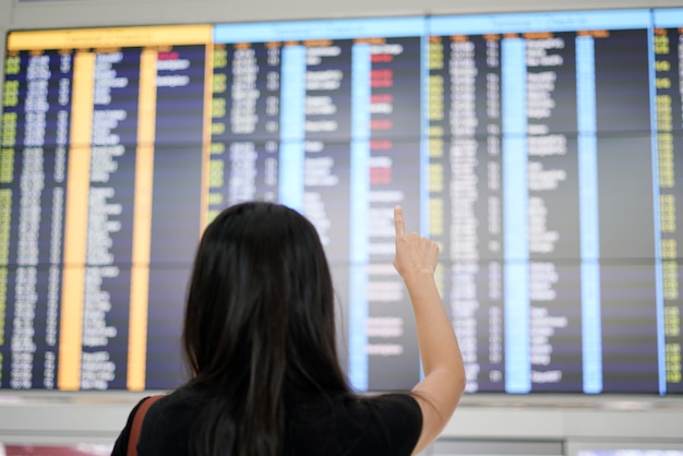 Kobieta podróżnik sprawdza lot odejść deskę przy lotniskowym terminal.
