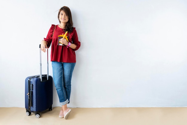 Kobieta podróżnik trzyma walizkę model samolotu paszport na szarym tle na białym tle