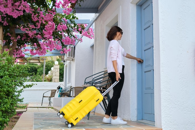 Kobieta podróżująca na zewnątrz z żółtą walizką otwierającą drzwi domu