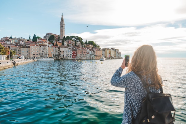 Kobieta podróżująca patrząca na miasto Rovinj z portu, robiąca zdjęcie telefonem