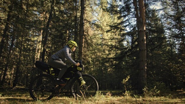 Kobieta podróżuje po mieszanym terenie cykloturystyka z rowerem bikepacking outdoor Podróżnik podróż z torbami rowerowymi Stylowa bikepacking rowerowa odzież sportowa w zielono-czarnej kolorystyce Magiczny las park