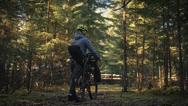 Kobieta podróżuje po mieszanym terenie cykloturystyka z rowerem bikepacking outdoor Podróżnik podróż z torbami rowerowymi Stylowa bikepacking rowerowa odzież sportowa w zielono-czarnej kolorystyce Magiczny las park