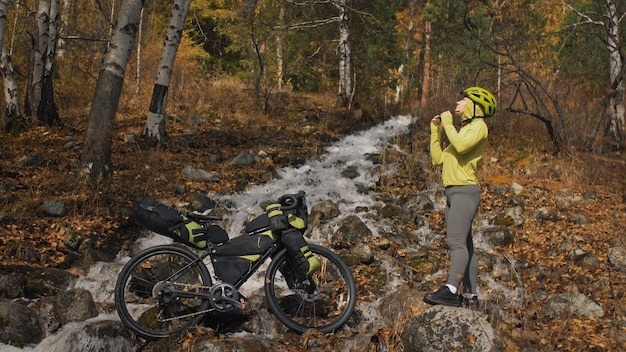Kobieta podróżuje po mieszanym terenie wycieczki rowerowe z bikepackingiem Podróżnik podróż z torbami rowerowymi Odzież sportowa w zielono-czarnej kolorystyce Wycieczka w magiczny jesienny leśny strumyk