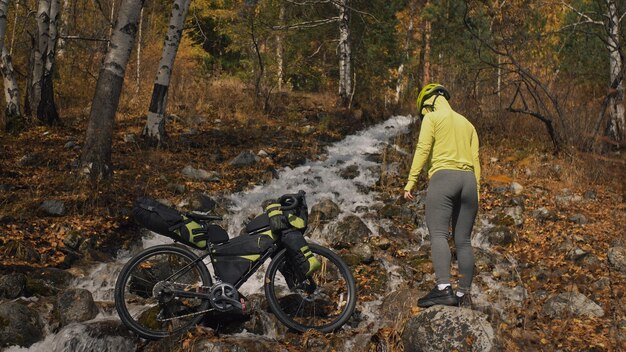 Kobieta podróżuje po mieszanym terenie wycieczki rowerowe z bikepackingiem Podróżnik podróż z torbami rowerowymi Odzież sportowa w zielono-czarnej kolorystyce Wycieczka w magiczny jesienny leśny strumyk